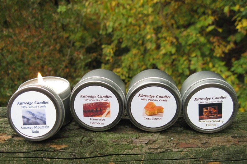 May include: Four silver candle tins with labels. The labels are white with black text and images. The candle scents are Smokey Mountain Rain, Tennessee Barbecue, Corn Bread, and Tennessee Whiskey Festival.