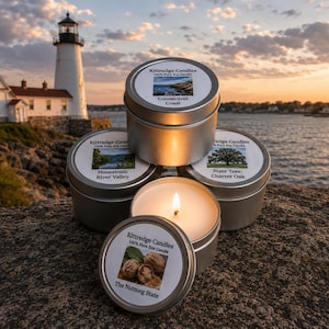 May include: Several silver tin candles with labels featuring scenic images and text, one lit with a flame. The labels read "Connecticut Coast", "Housatonic River Valley", "State Tree: Charter Oak", and "The Nutmeg State". A lighthouse and ocean are in the background.
