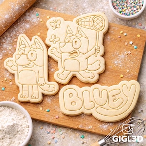 May include: Three cookie cutters in the shape of the cartoon character Bluey. One cutter is the word "Bluey", and the other two are the character in different poses. The cutters are on a wooden cutting board with flour and sprinkles.
