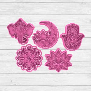 Puede incluir: Colección de cinco cortadores de galletas rosas de varias formas. Las formas incluyen una cabeza de elefante, una luna creciente con una flor de loto, una mano de Hamsa, un mandala floral y una flor de loto. Los cortadores son de plástico.
