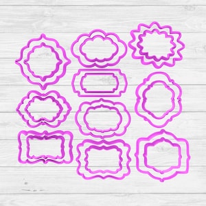 May include: A collection of eleven pink cookie cutters in various ornate frame shapes. The cutters are made of plastic and are arranged on a light wood-grain surface. The designs include rectangular, oval, and scalloped edges, suitable for baking and crafting.