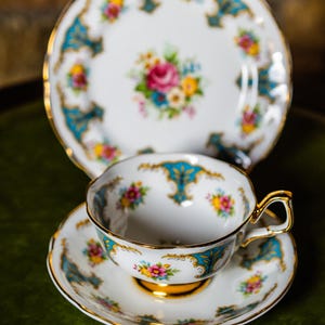 Può includere: Una tazza da tè e un piattino bianchi con un motivo floreale blu e oro. La tazza e il piattino hanno un bordo ondulato.