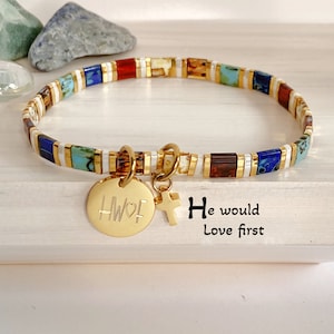 May include: A gold bracelet with colorful beads and a charm that says "HWF" with a heart and a cross charm. The bracelet is on a white surface with the text "He would Love first".