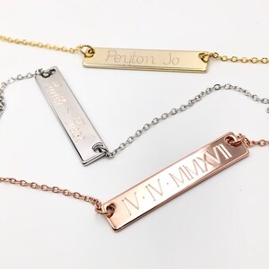 May include: Three gold bar necklaces with different engravings. The top necklace has the name "Peyton Jo" engraved on the bar. The middle necklace has the words "Smith & Beck" engraved on the bar. The bottom necklace has the Roman numerals "IV.IV.MMXVI" engraved on the bar.