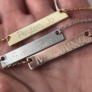May include: Three gold bar necklaces with different engravings. The top necklace has the name "Peyton Jo" engraved on it. The middle necklace has the words "Faith > Fear" engraved on it. The bottom necklace has the Roman numerals "IV.IV.MMXVI" engraved on it.