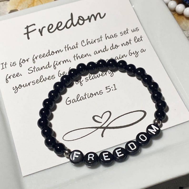 May include: Black beaded bracelet with the word "FREEDOM" spelled out in white letters. A card behind the bracelet reads "Freedom" and includes a Bible verse from Galatians 5:1.