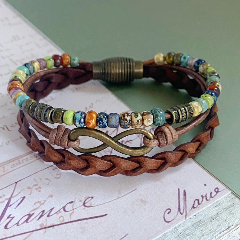 May include: A multi-strand leather bracelet with a colorful beaded row and an infinity symbol charm. The bracelet has a brown leather strap with a braided design.