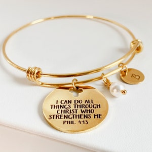 Può includere: Braccialetto rigido in oro con un ciondolo che recita "Posso fare tutto in Cristo che mi fortifica Fil 4:13". Il ciondolo ha anche un piccolo taglio a forma di croce. Il braccialetto ha un ciondolo di perla e un ciondolo con la lettera "B".