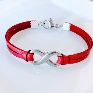 May include: Red leather bracelet with a silver infinity symbol charm.
