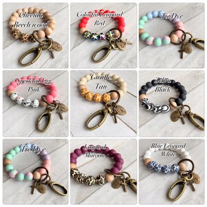 Op de afbeelding: Negen verschillende sleutelhangers van siliconen en houten kralen met een metalen sluiting en bedel. De sleutelhangers hebben verschillende patronen en kleuren, waaronder cheetah, luipaard, giraffe, zebra, tie-dye, gevlekt ei en blauwe luipaard.