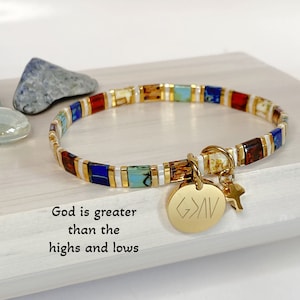 May include: Gold beaded bracelet with colorful square beads and a gold charm with the words "God is greater than the highs and lows".