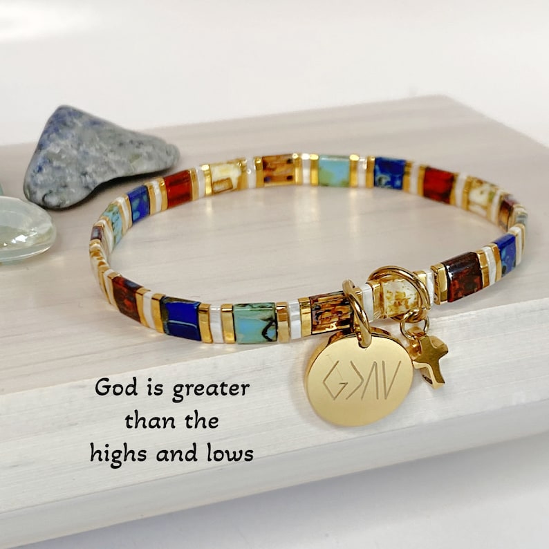 May include: Gold beaded bracelet with colorful square beads and a gold charm with the words "God is greater than the highs and lows".