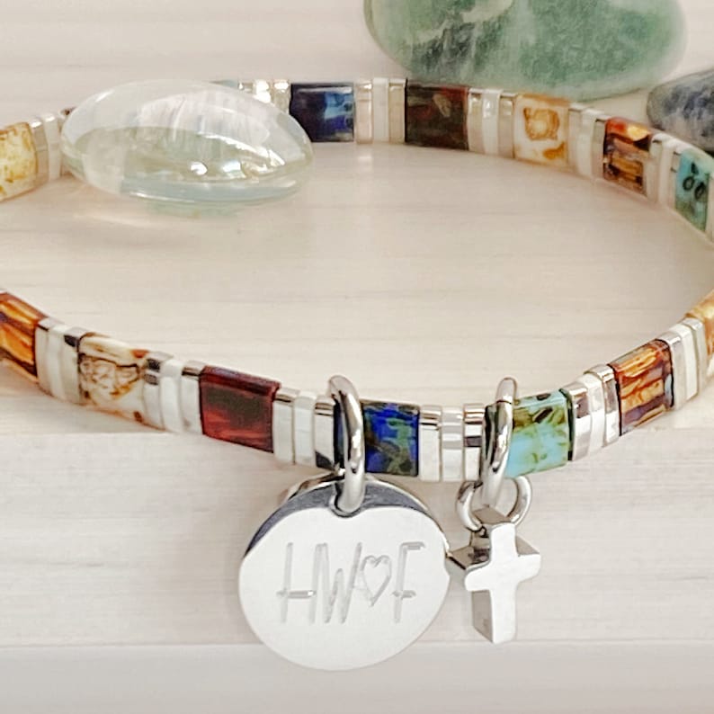 May include: A silver bracelet with colorful square beads and two charms. One charm is a round disc with the initials "HWF" and a heart symbol. The other charm is a silver cross.