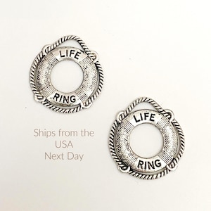 May include: Two silver-toned life ring charms. Each charm features the words "LIFE" and "RING" in black lettering. The charms have a rope-like border and a loop at the top. The background is white.