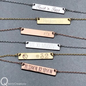May include: Five gold, silver, and rose gold bar necklaces with different engraved text. The text on the necklaces reads "Faith > Fear", "Peyton Jo", "VII.XI.MMXIV", a basketball with the number "32", and "39.3244'N, 82.1014'W".