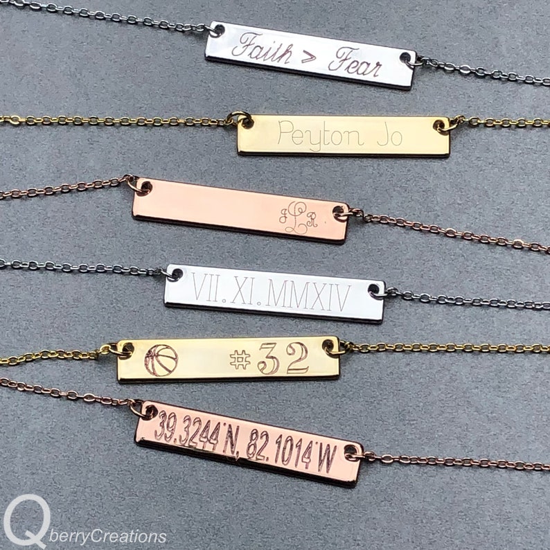 May include: Five gold, silver, and rose gold bar necklaces with different engraved text. The text on the necklaces reads "Faith > Fear", "Peyton Jo", "VII.XI.MMXIV", a basketball with the number "32", and "39.3244'N, 82.1014'W".