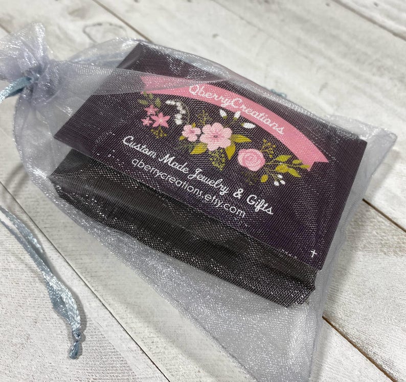 May include: A black and white card with pink floral designs and the text "Qberry Creations Custom Made Jewelry & Gifts qberrycreations.etsy.com" is inside a silver mesh bag.