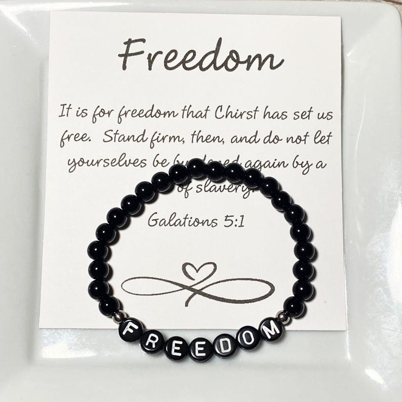 May include: A black beaded bracelet with the word "FREEDOM" spelled out in white letter beads. The bracelet is displayed on a white card with the word "Freedom" and a Bible verse printed on it.
