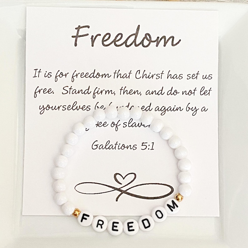 May include: White beaded bracelet with the word "FREEDOM" spelled out in white letter beads. The bracelet is displayed in front of a white card with the word "Freedom" and a Bible verse.