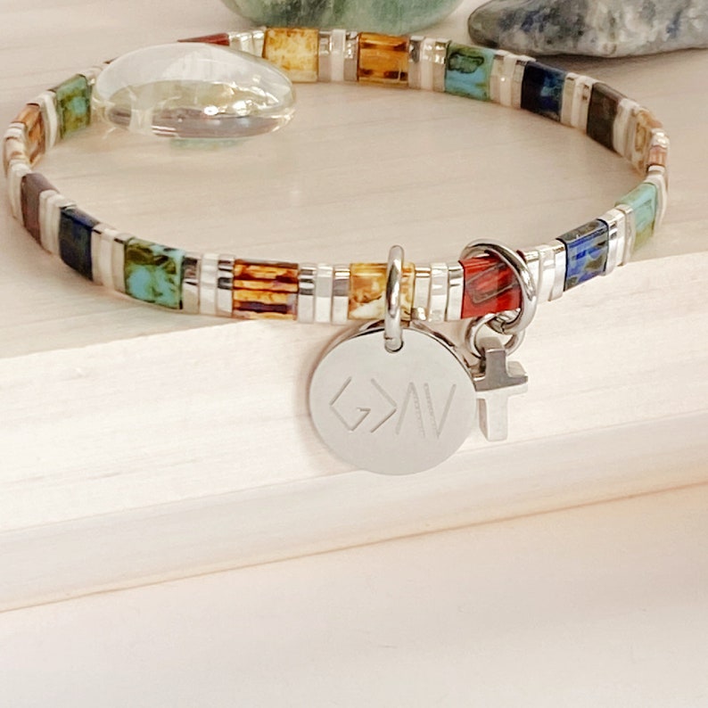 May include: A colorful beaded bracelet with a silver charm that says "G>A" and a small silver cross charm.