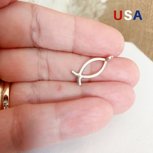 May include: A silver-toned, open-loop, fish-shaped charm pendant. The pendant is small and delicate, and is perfect for adding a touch of faith to jewellery.