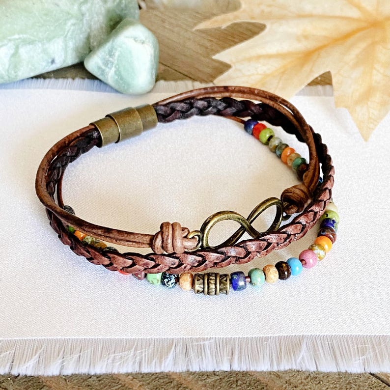 May include: A multi-strand leather bracelet with an infinity charm and colorful beads. The bracelet is brown and has a braided leather design.