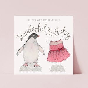 A square card on a pink  background. The card has an illustration of a penguin stood next to a pink party dress which can be cut out and put on the penguin. Hand lettering at the top says Put your party dress on and have a wonderful birthday.