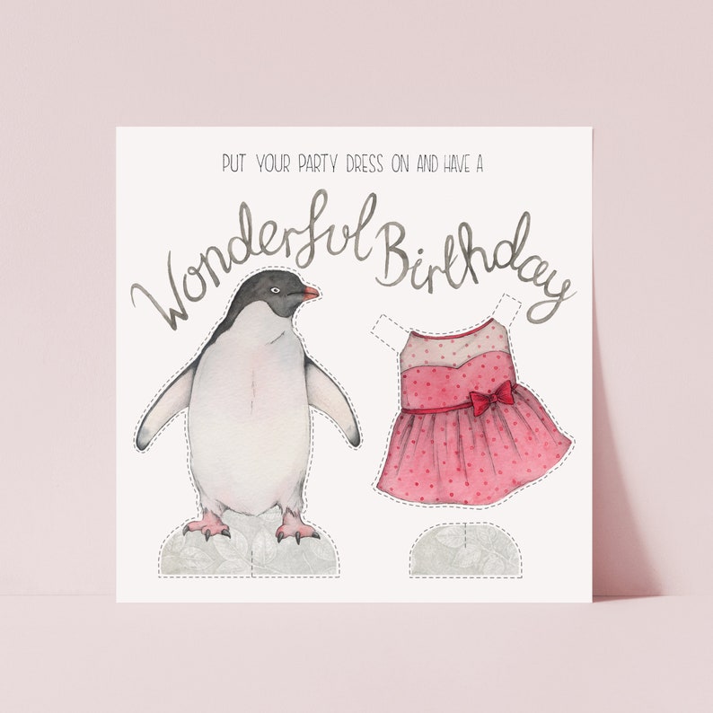 A square card on a pink  background. The card has an illustration of a penguin stood next to a pink party dress which can be cut out and put on the penguin. Hand lettering at the top says Put your party dress on and have a wonderful birthday.