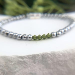 Op de afbeelding: Een zilveren armband met een rij groene edelsteen kralen.