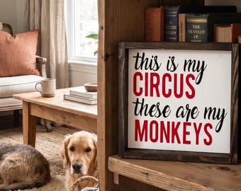 May include: A framed sign with the text "this is my CIRCUS these are my MONKEYS" in black and red. The sign is on a wooden shelf with books. A golden retriever dog is in the foreground. The sign is in a room.