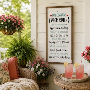 May include: A rectangular wooden sign with a white background and dark brown frame, featuring the text "welcome DECK RULES" followed by a list of phrases including "SIT AND RELAX," "APPRECIATE TODAY," and "TREASURE FAMILY TIME" in black and teal.