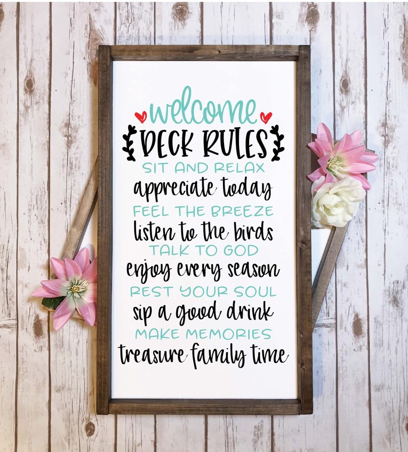 May include: A rectangular wooden sign with a dark brown frame and a white background featuring black and teal text that reads: welcome DECK RULES SIT AND RELAX appreciate today FEEL THE BREEZE listen to the birds TALK TO GOD enjoy every season REST YOUR SOUL sip a good drink MAKE MEMORIES treasure family time.