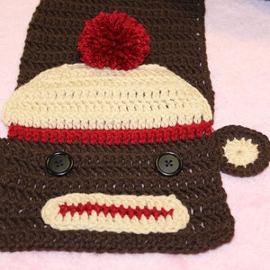May include: Crocheted monkey scarf with a brown face, red pom-pom hat, and black button eyes.
