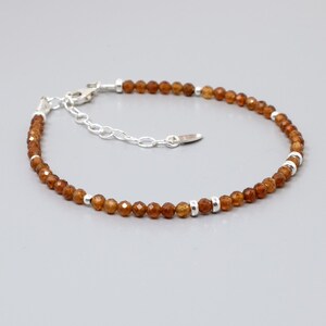 May include: A delicate bracelet featuring small, faceted, orange-brown gemstone beads. The bracelet has a silver-colored clasp and small silver-colored spacer beads. The bracelet is designed to be adjustable.