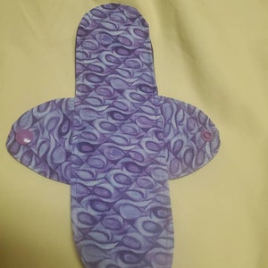 May include: Purple and white patterned reusable cloth pad with two purple snaps on the sides.