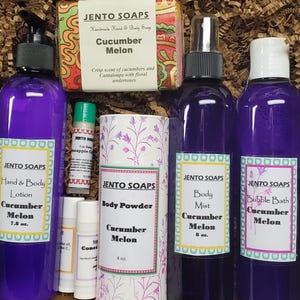 May include: A gift box filled with a variety of bath and body products in a cucumber melon scent. The box includes a bar of soap, a bottle of hand and body lotion, a bottle of body mist, a bottle of bubble bath, and a container of body powder. All products are labeled with the brand name "Jento Soaps".