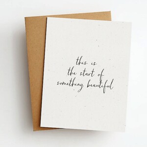 Op de afbeelding: Een witte kaart met de tekst "This is the start of something beautiful" geschreven in zwarte cursieve letters.