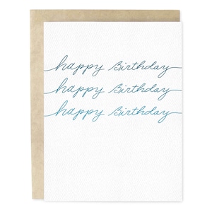 May include: A white birthday card with the words "happy Birthday" written three times in teal script. The card is inside a light brown envelope. The card has a textured surface.