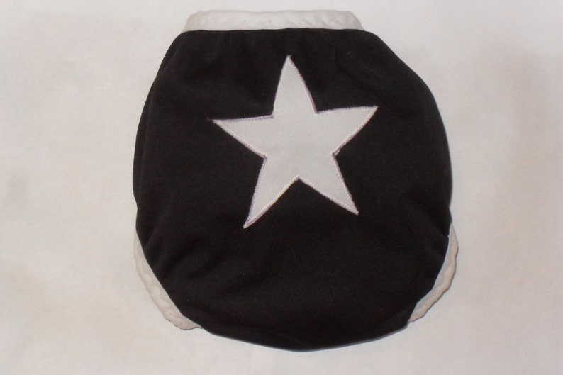 May include: Black cloth diaper with a white star in the center. The diaper has white trim around the edges.