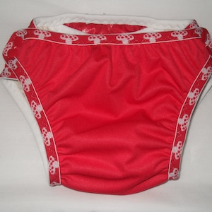 May include: Red swim diaper with white trim featuring a repeating pattern of small white mushrooms.