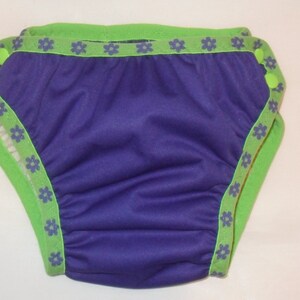 May include: Purple swim diaper with green and blue trim and a floral pattern.