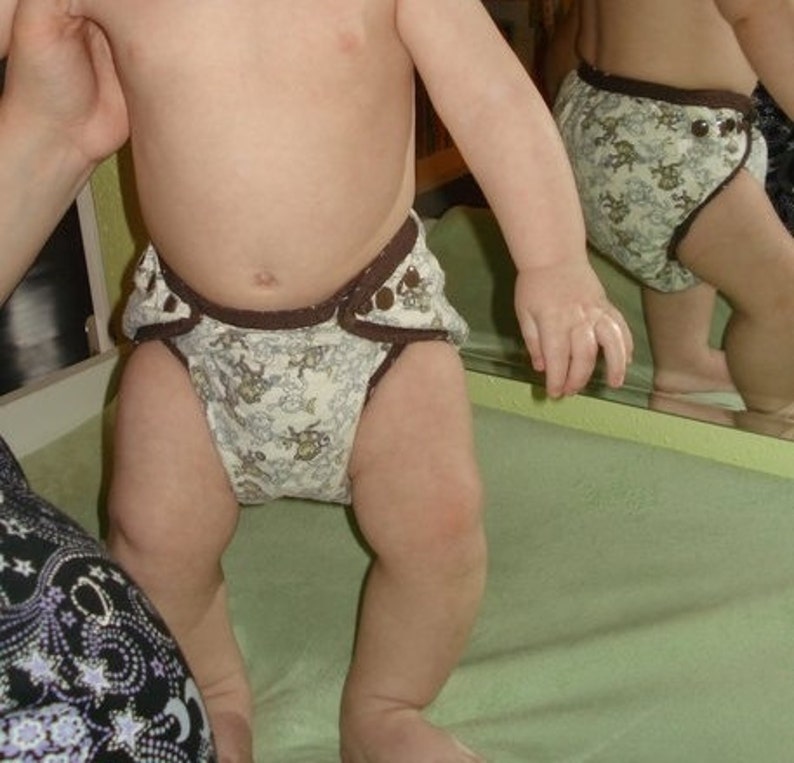 May include: A baby wearing a brown and white patterned cloth diaper with a brown elastic waistband.