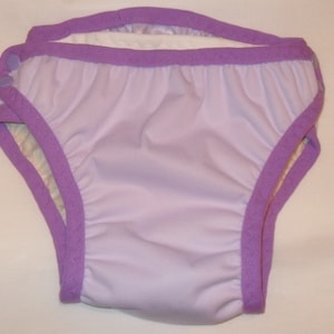 May include: Purple swim diaper with white lining and snap closure. The diaper is made of a soft, waterproof material.