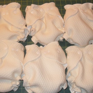 Puede incluir: Seis pa&ntilde;ales de tela blancos doblados y dispuestos en fila sobre una superficie a cuadros verde y blanca.