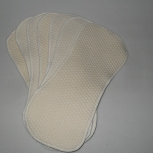 Puede incluir: Un paquete de diez insertos de pañales de tela de color crema con textura acolchada y ribete blanco.