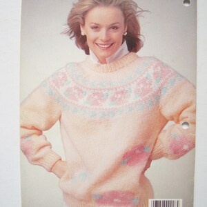 Peut inclure: Un pull rose avec un motif blanc et bleu. Le pull est fabriqu&eacute; par Patons.