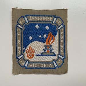 Peut inclure: Écusson brodé avec un motif bleu, blanc et orange. L'écusson comporte les mots "Jamboree", "Pan Pacific", "Yarra Brae" et "Victoria". Le motif comprend une torche, des étoiles et un fleur-de-lis.
