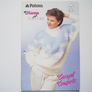 Peut inclure: Un pull en tricot blanc et bleu avec un motif de flocon de neige. Le pull est port&eacute; par une femme aux cheveux bruns courts. Le texte "Diana and Davina" est imprim&eacute; sur la page. Le texte "Casual Comforts" est imprim&eacute; en rose sur la page.
