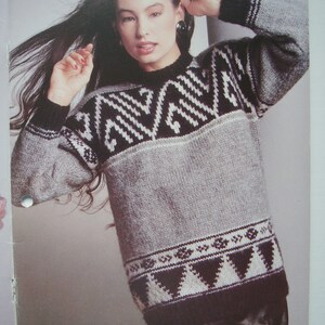 Peut inclure: Un pull en tricot gris et noir avec un motif g&eacute;om&eacute;trique. Le pull a un col rond et des manches longues.