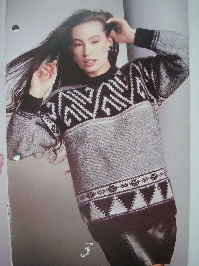 Peut inclure: Un pull en tricot gris et noir avec un motif g&eacute;om&eacute;trique. Le pull a un col rond et des manches longues.
